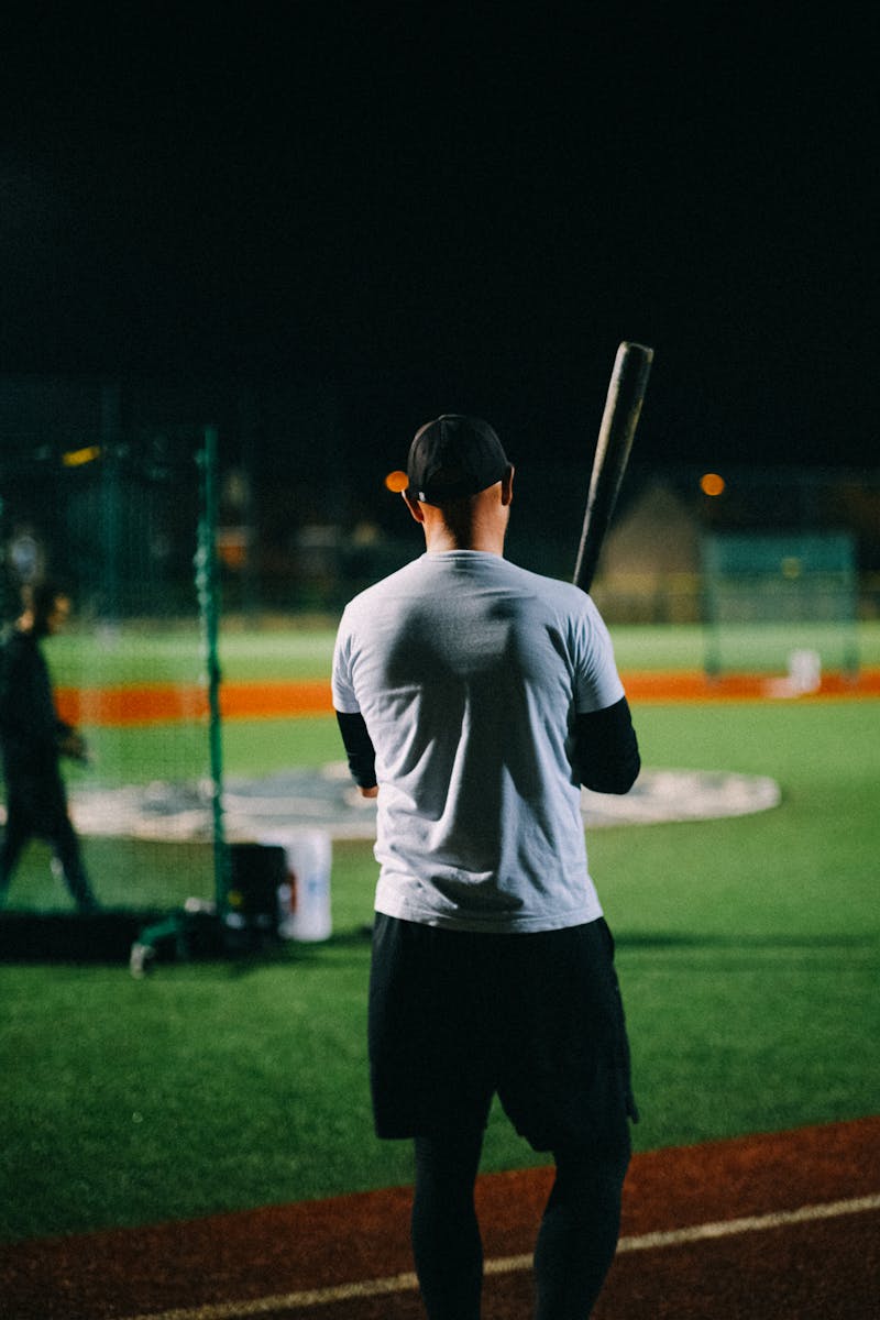 A baseball player stands with a bat on a sports field at night.