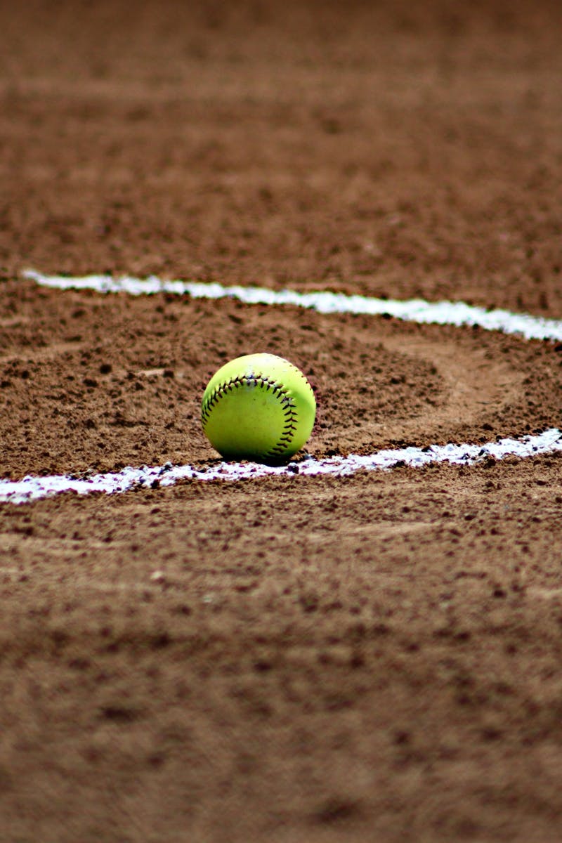 A softball resting on a dirt field with chalk lines marking the infield.
